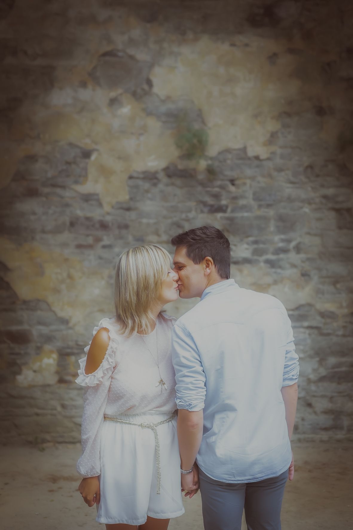 Romantisch koppel in witte outfits in elkaars armen bij rustieke stenen muur