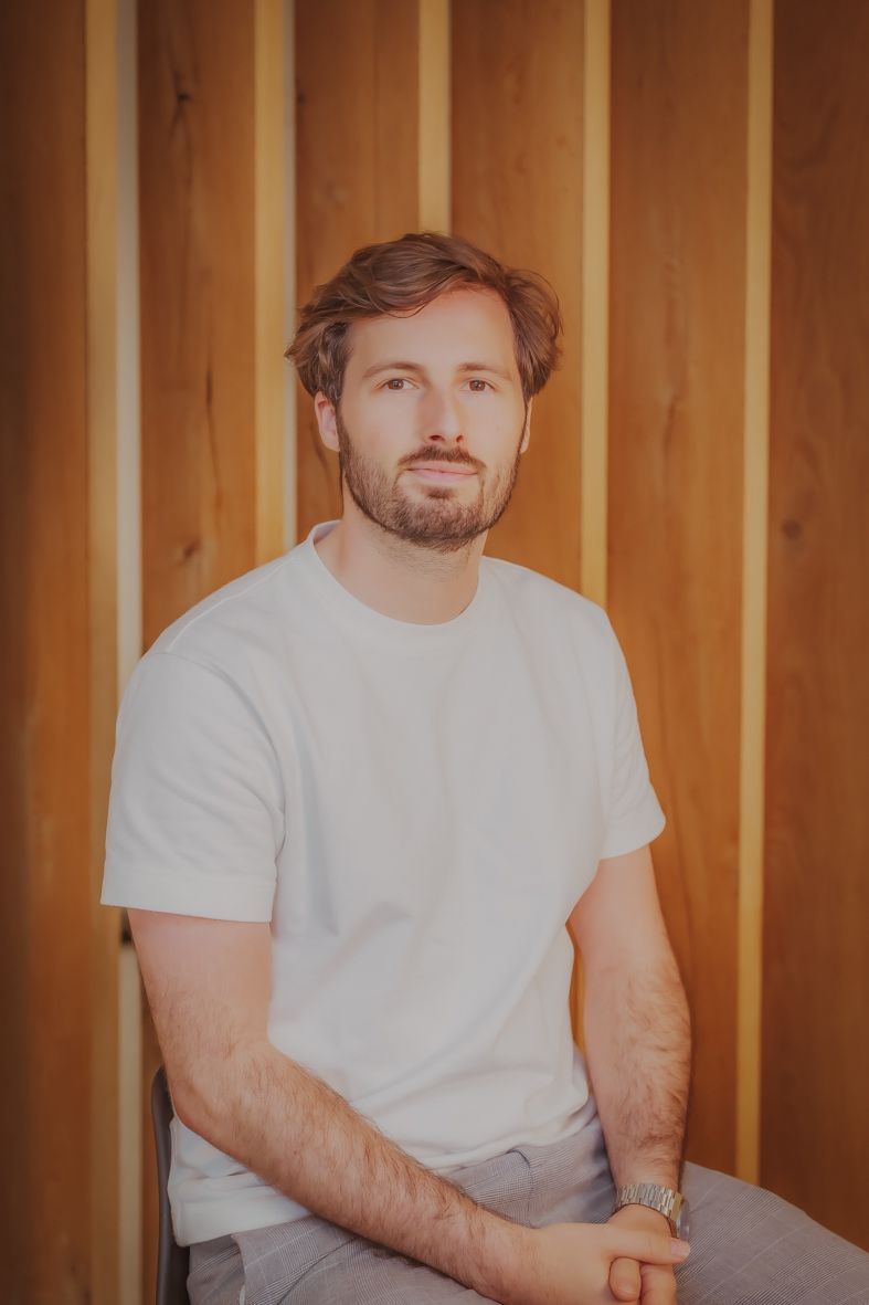 Persoon in wit t-shirt zit voor houten lattenwerk in warm licht