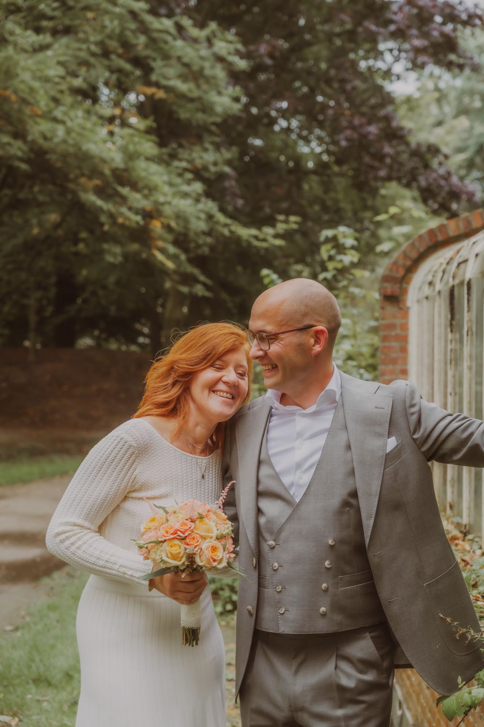 Koppel deelt een vrolijk moment buiten, bruid in wit met perzikkleurig boeket