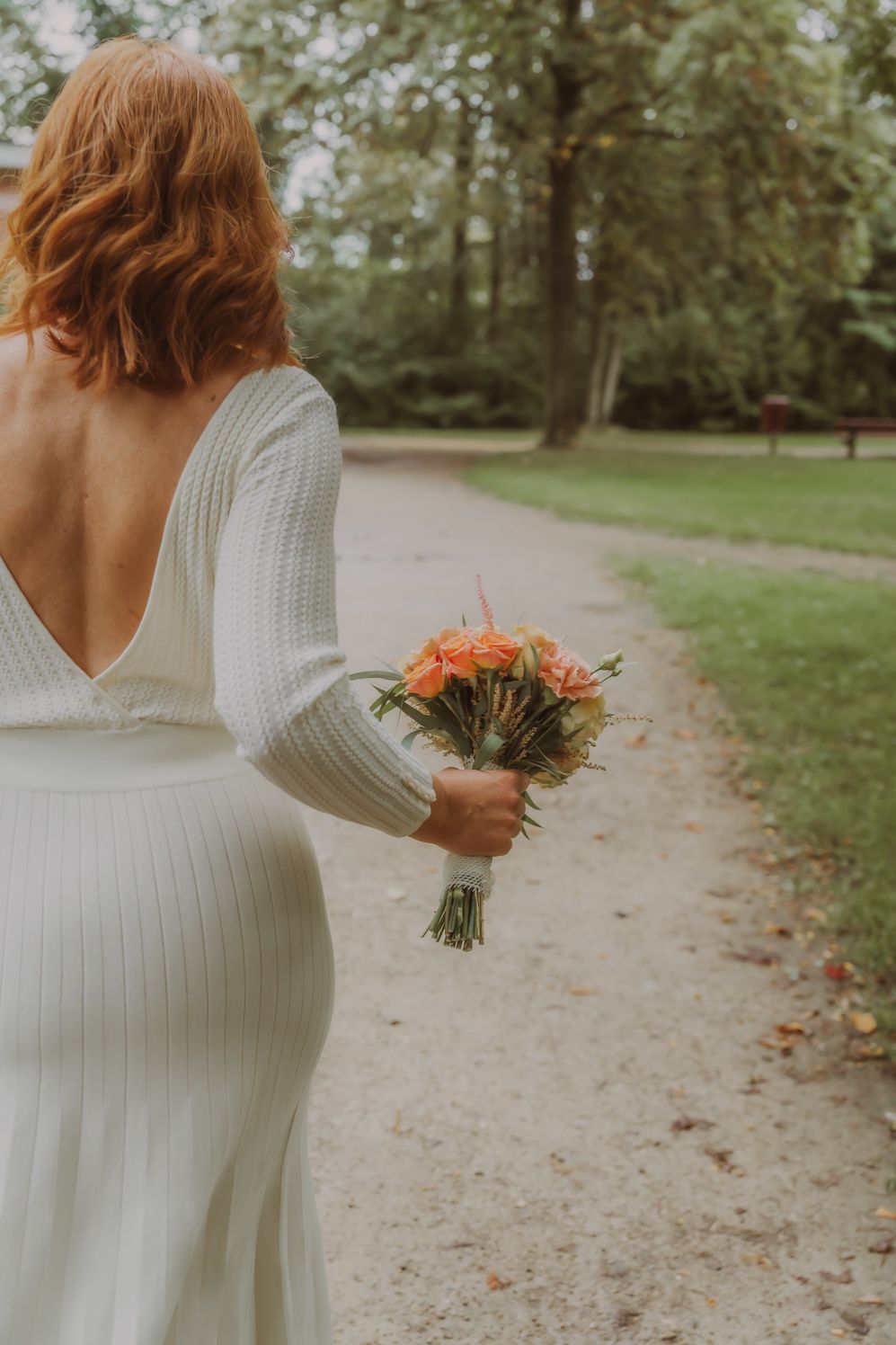 Bruid in witte jurk wandelt met perzikkleurig boeket