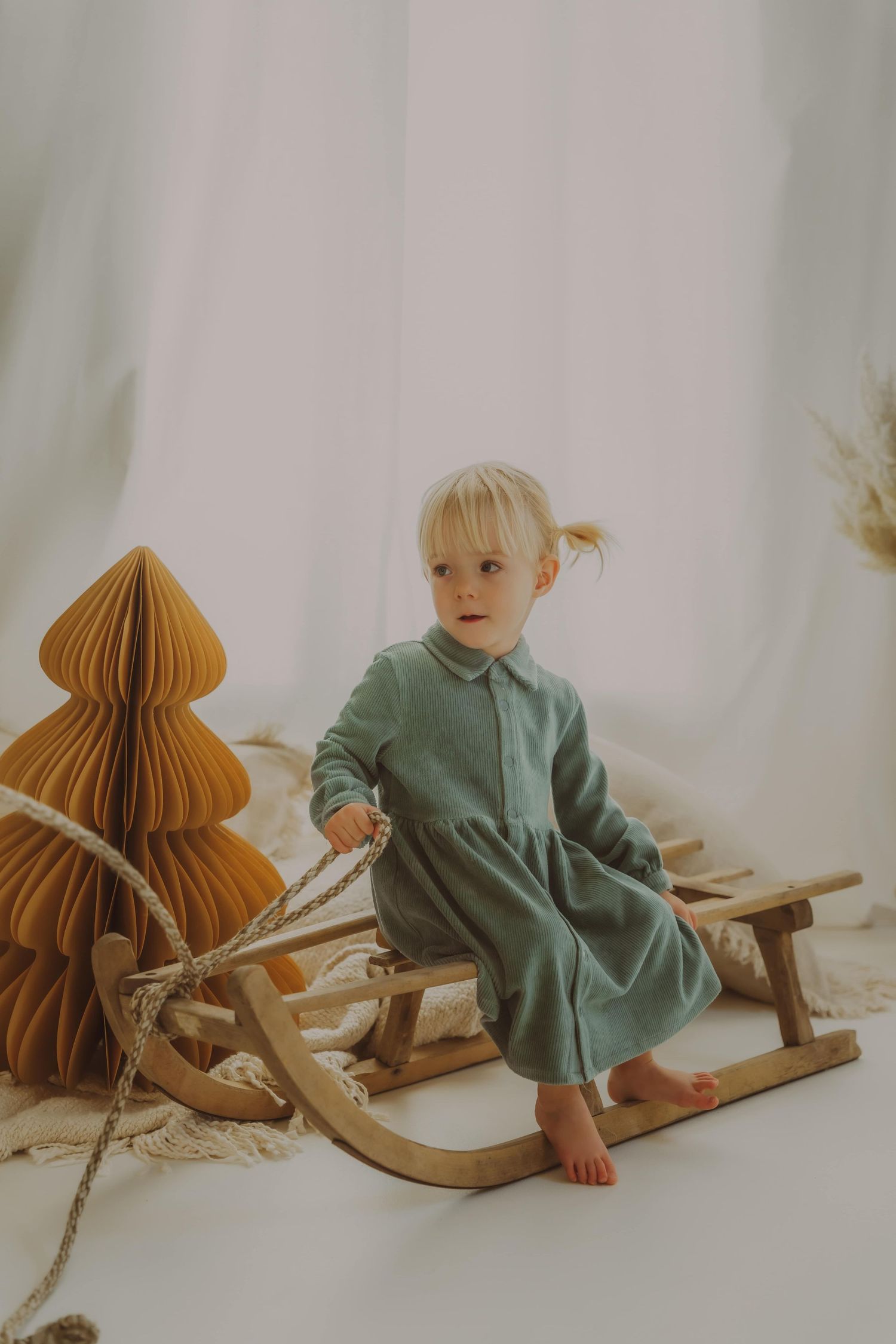 Kind in saliegroen jurkje op een houten schommelpaard