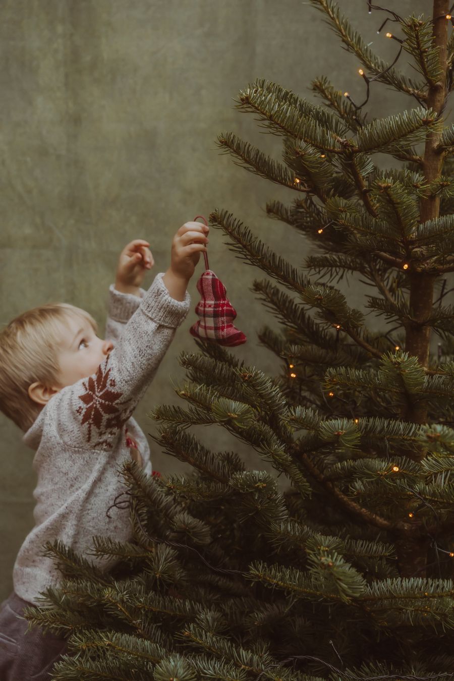 Kind in witte trui hangt kerstballen in de boom