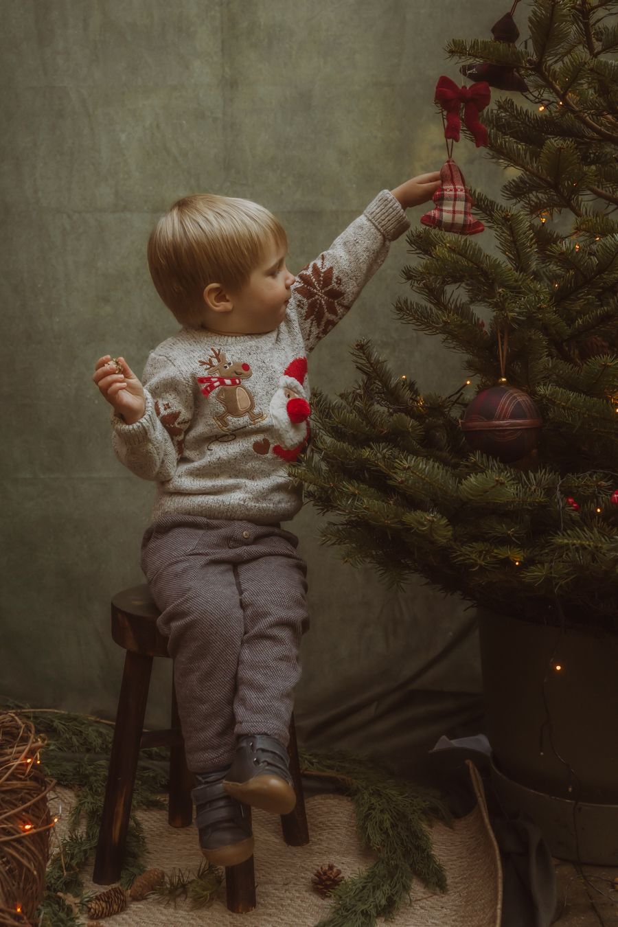 Klein kind versiert kerstboom staand op een houten krukje