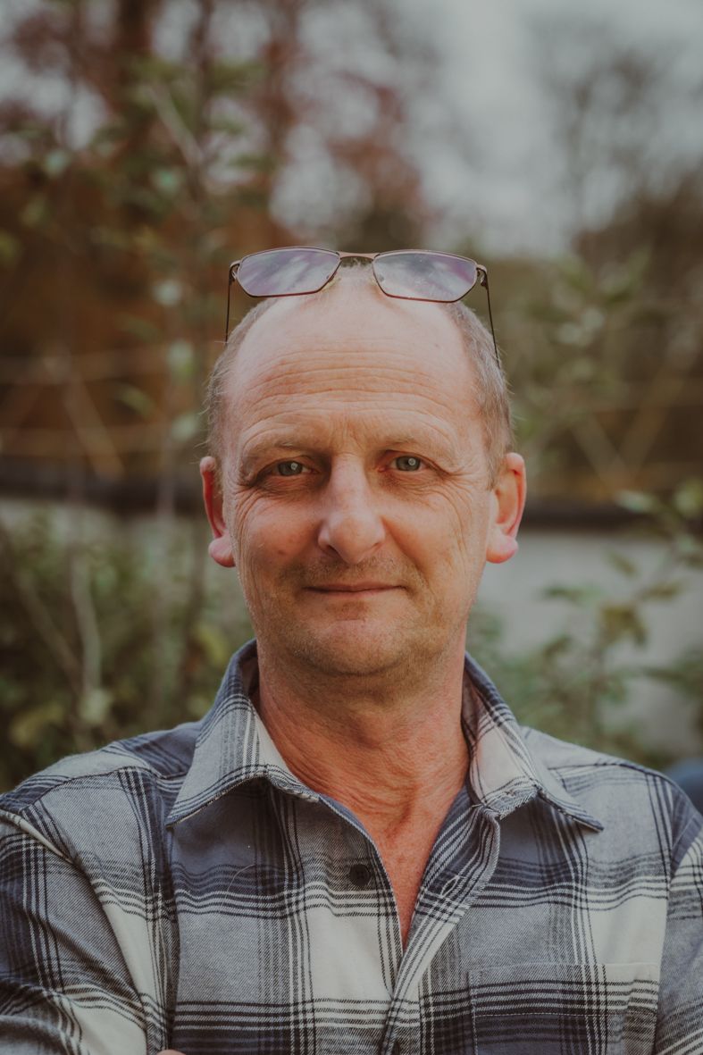 Persoon in geblokt shirt en bril lacht warm in buitenatmosfeer