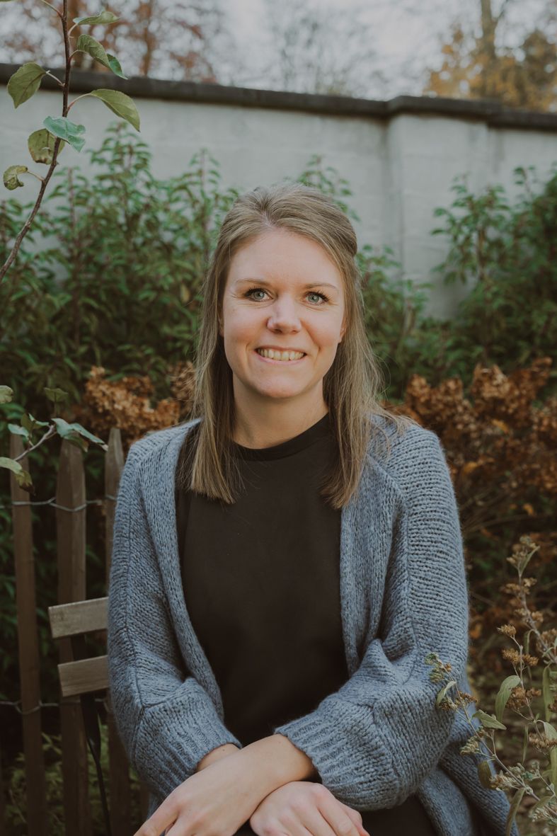 Persoon in grijze cardigan zit buiten bij herfstachtergrond en houten hek