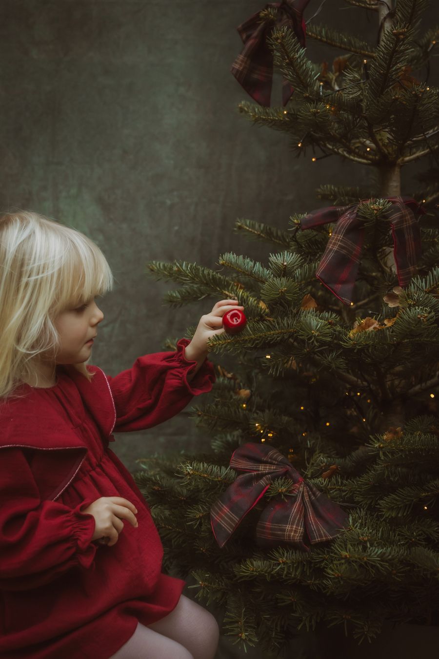 Kind in rode trui hangt kerstballen in sfeervolle omgeving