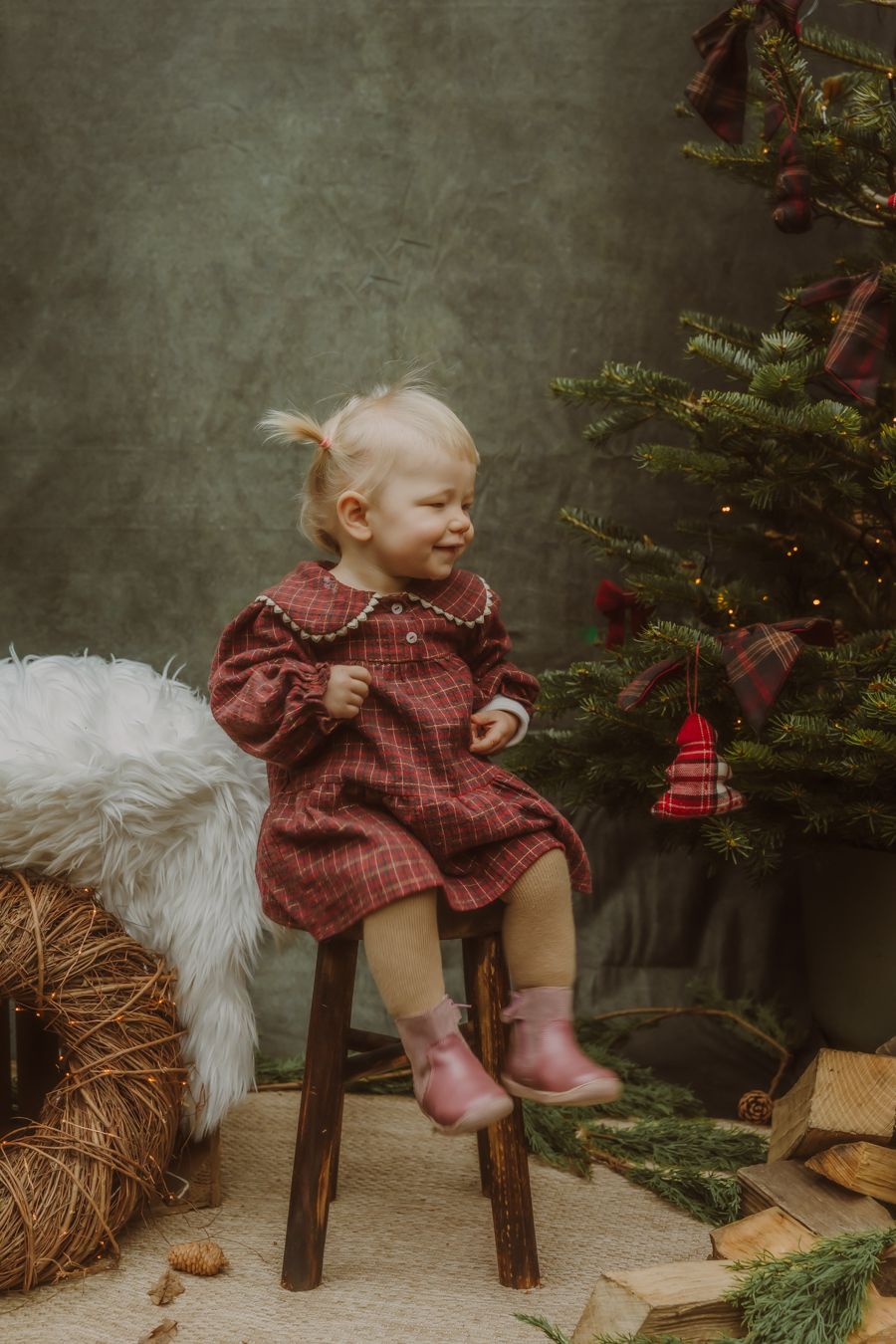 Kind in geruite jurk bij kerstboom met cadeautjes